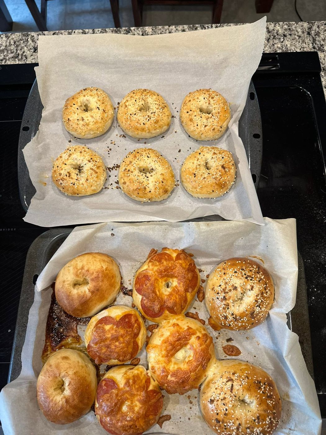 Two trays of homemade sourdough bagels, some topped with pepperoni and cheese